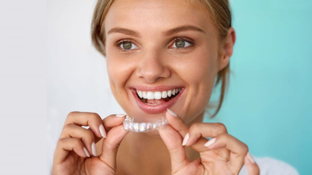 A Woman Smiling, Holding An Invisalign